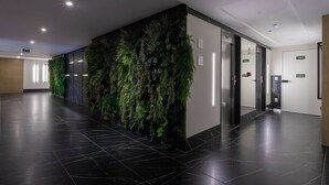 En moderne gang med sorte fliser, en grøn væg med hængende planter og to elevatorer.