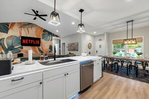 A modern kitchen with a built-in dishwasher, a large island with a sink, and a dining area with a long table and chairs. - Family Retreat, Fire Pit, Games, Close to Ft Moore (Columbus)