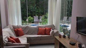 A living room with a sofa, armchair, and TV stand. - 4-bedroom house in delightful Riviera, 15 minute walk to the beach and the mall. (Bertioga)