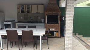 An outdoor kitchen with a brick oven, dining table, and chairs. - 4-bedroom house in delightful Riviera, 15 minute walk to the beach and the mall. (Bertioga)