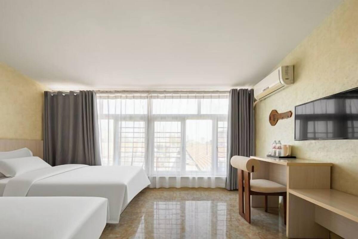 Ein Hotelzimmer mit zwei Betten, einem Schreibtisch, einem Stuhl, einem Fernseher und einem Fenster mit Vorhängen.
