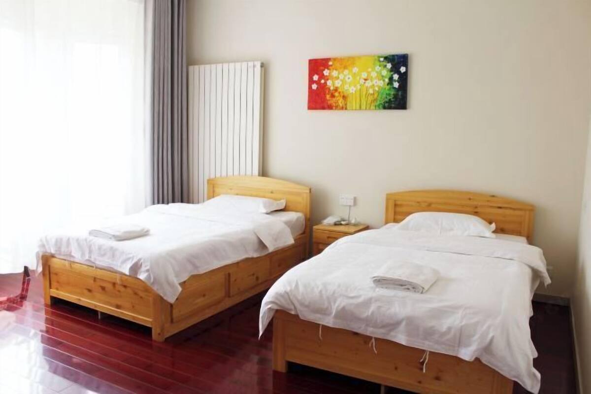 Zwei hölzerne Betten mit weißer Bettwäsche, ein Heizkörper und ein farbenfrohes Bild an der Wand.