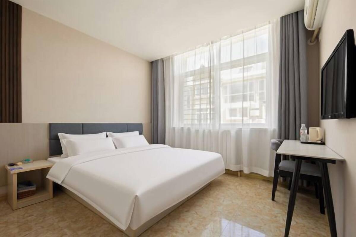 Ein Hotelzimmer mit Bett, Schreibtisch, Stuhl, Fernseher und einem Fenster mit Vorhängen.