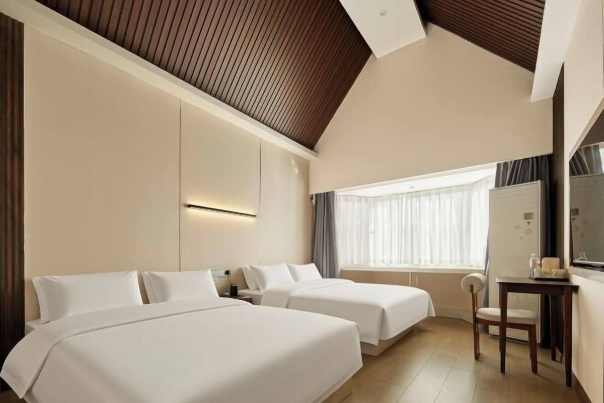 Ein Hotelzimmer mit zwei Betten, einem Schreibtisch, einem Stuhl, einem großen Fenster und einer Holzbalkendecke.