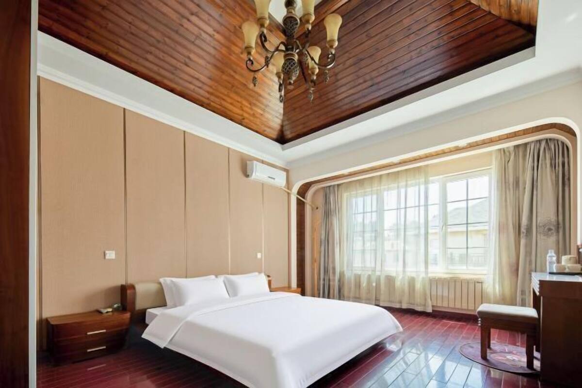 Ein Hotelzimmer mit Holzboden, einem Bett, einem Schreibtisch und einem Fenster mit Vorhängen.