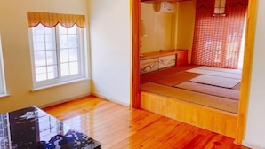 Une pièce avec un plancher en bois, un espace recouvert de tatamis, une fenêtre avec un rideau et une petite table.