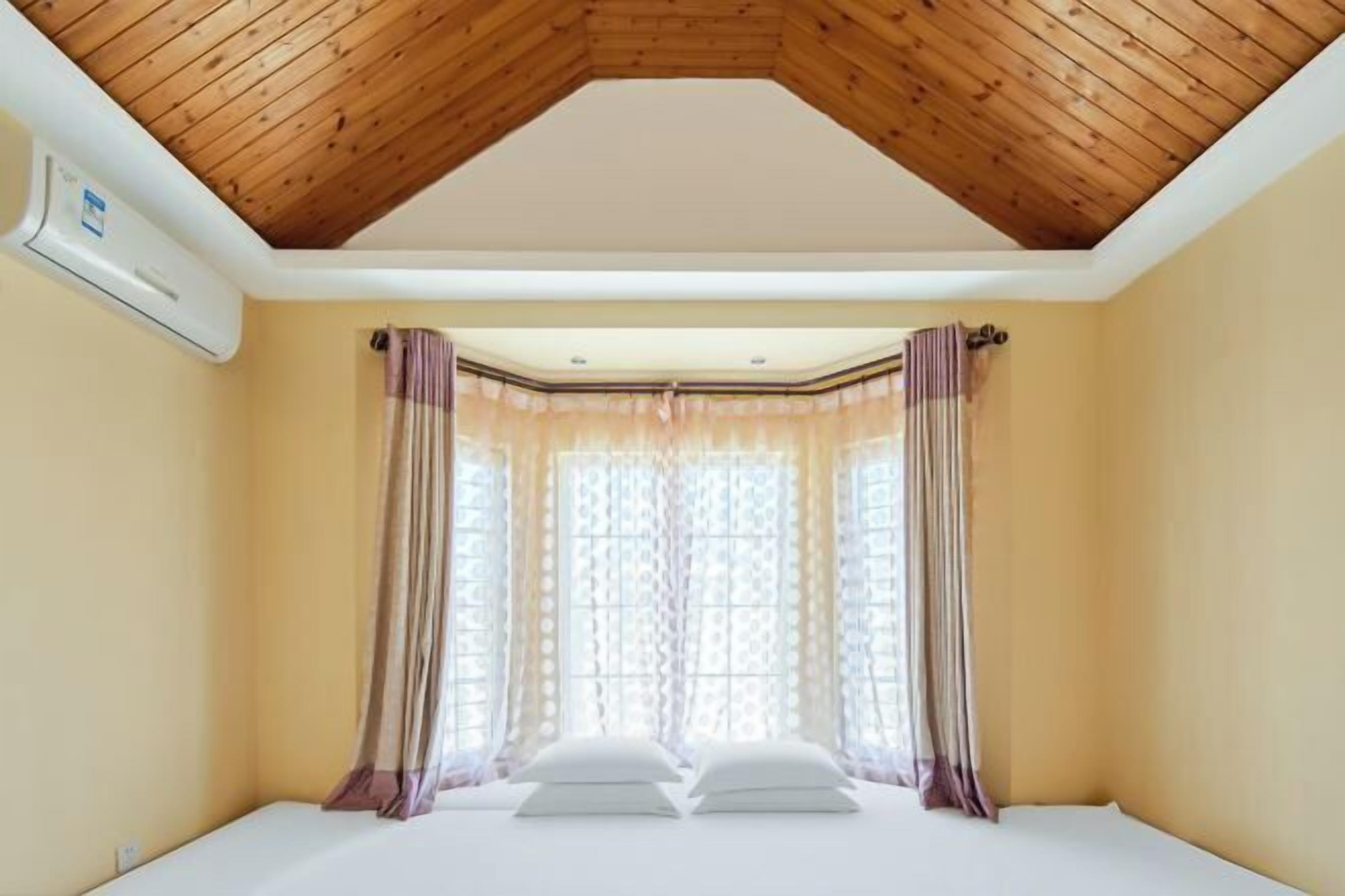 A bedroom with a sloped ceiling, a bed, curtains, and a window.