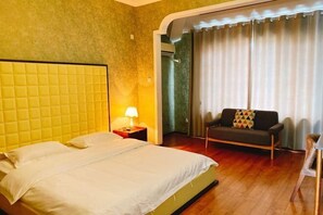 Ein Hotelzimmer mit Bett, Nachttisch, Sofa und einem Fenster mit Vorhängen.