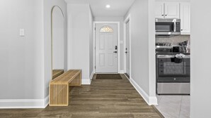 A hallway with a bench, a door with a stained glass window, and a kitchen with stainless steel appliances.