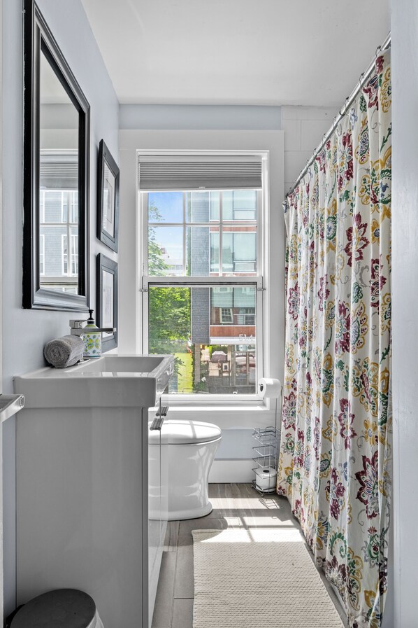 A bathroom with a large window, a toilet, a sink, and a shower curtain.