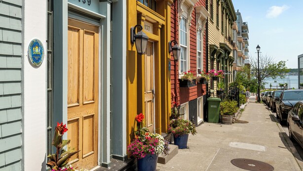 A row of colorful townhouses with numbered doors, a sidewalk, parked cars, and a body of water in the background. - Historic 2 bedroom central down town location near waterfront - #3 (Halifax)