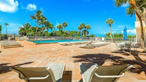 A poolside area with lounge chairs, a swimming pool, and palm trees. - Beachfront Condo With Pool, Tennis and Fitness Center (Marco Island)