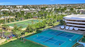 A tennis court surrounded by greenery and a multi-story building with satellite dishes. - Beachfront Condo With Pool, Tennis and Fitness Center (Marco Island)