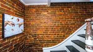 A staircase with a brick wall and a painting of hands reaching for an apple.