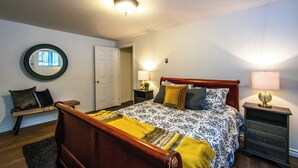 A bedroom with a wooden bed, a bedside table, a nightstand, a mirror, and a door.