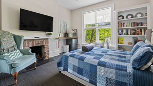 A bedroom with a fireplace, a television, a bookshelf, and a large window. - Halifax Old South District Library Suite (Halifax)