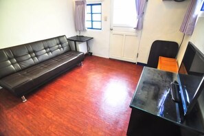 A room with a black leather sofa, a small table, a black TV stand, and a door with a window. - Peng Hu Dream (Penghu)