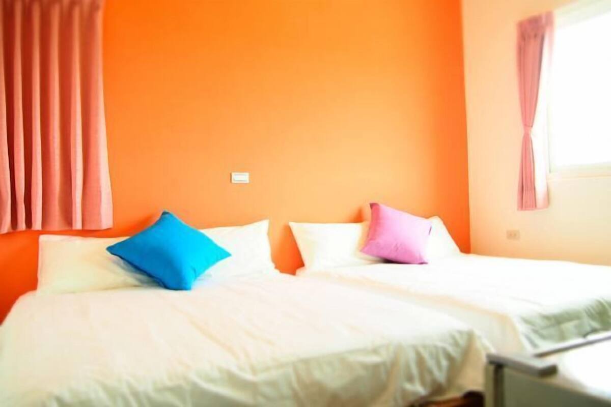 A hotel room with two beds, orange walls, and a window with curtains.