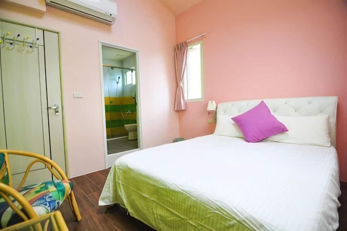 A bedroom with a bed, a chair, a wardrobe, and a bathroom visible through an open door.