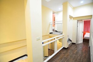 A hallway with a glass railing, a staircase, and a bed with red curtains. - Peng Hu Dream (Penghu)
