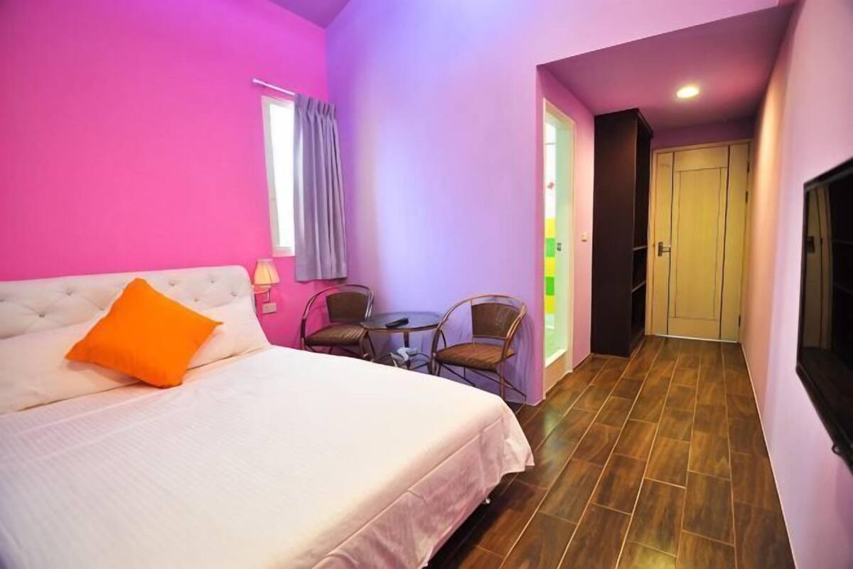 A hotel room with a bed, a chair, a small table, and a door.