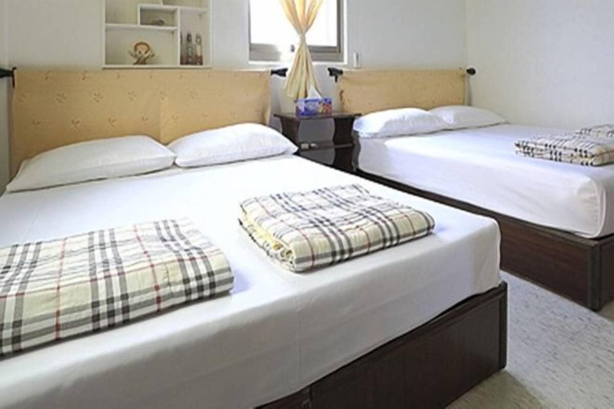 A hotel room with two beds, a bedside table, a mirror, and a window with curtains.