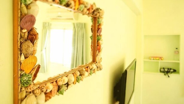 A mirror with a seashell frame, a television, and a shelf with items in a room with yellow walls. - Peng Hu Dream (Penghu)