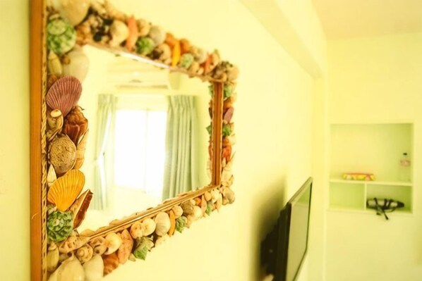 A mirror with a seashell frame, a television, and a shelf with items in a room with yellow walls. - Peng Hu Dream (Penghu)