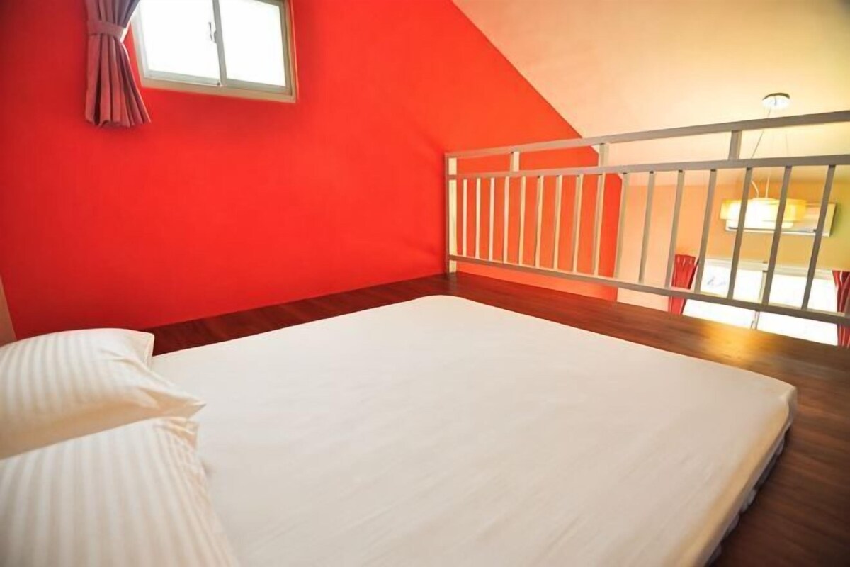 A room with a bed, a window with curtains, a white railing, and a view of the outside.
