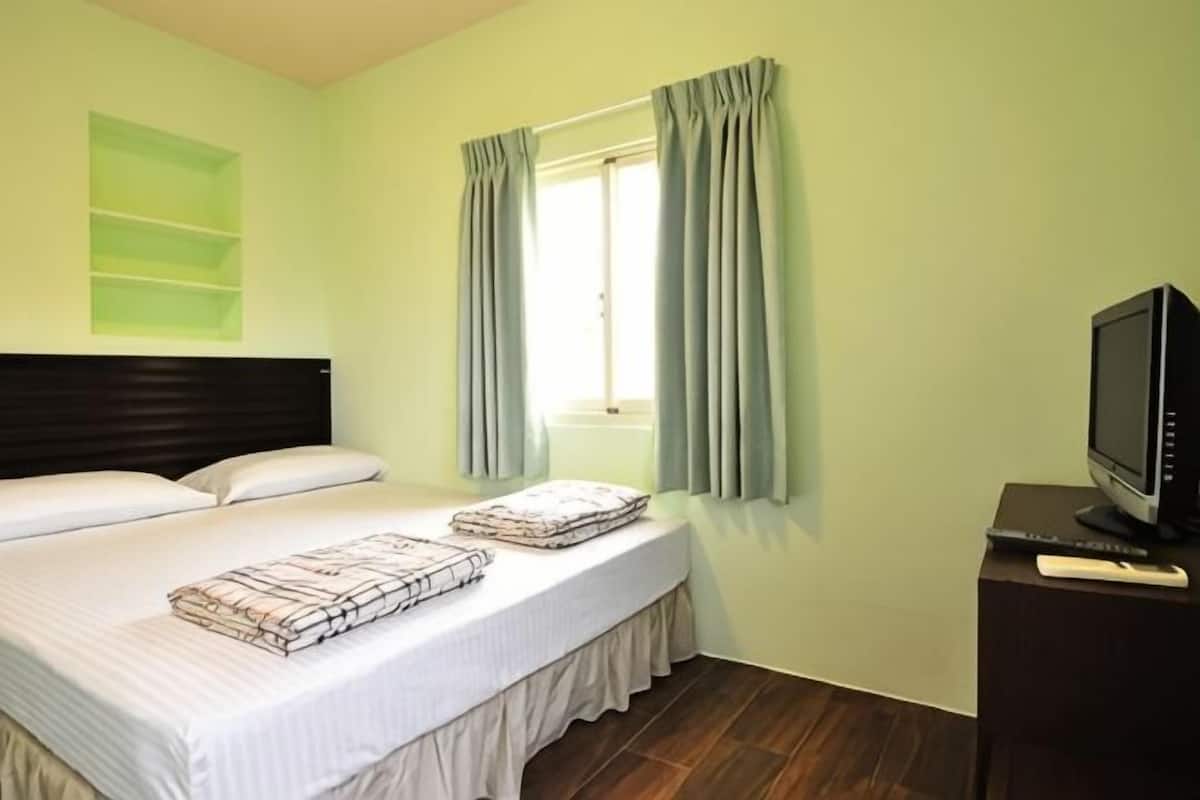 A hotel room with a bed, a television on a stand, and a window with curtains.