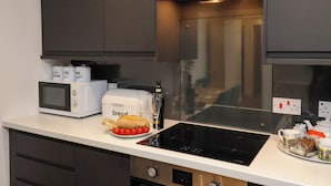 A modern kitchen with dark cabinets, a microwave, a bread maker, and a glass of wine on the counter. - The Arches (Whitby)