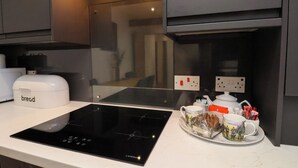 A kitchen with a black induction cooktop, a white bread maker, and a coffee maker on the counter. - The Arches (Whitby)