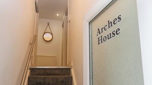 A staircase leading to a door labeled "Arches House" with a textured wall and a hanging light fixture. - The Arches (Whitby)