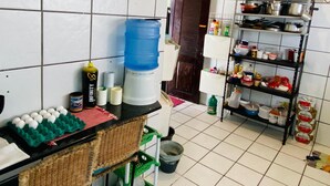 Een keuken met een betegelde spatwand, een waterdispenser, een plank met keukengerei en een rieten stoel.