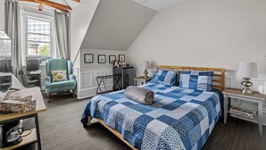 A bedroom with a sloped ceiling, a bed with a blue and white quilt, a desk with a laptop, a chair, and a window with curtains. - Chic Loft suite with WiFi & AC in historic downtown town Halifax near waterfront (Halifax)