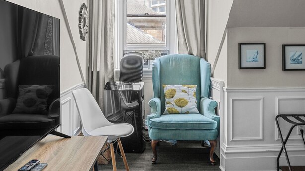 A cozy room with a wooden ceiling, a comfortable armchair, a desk, and a large window with curtains. - Chic Loft suite with WiFi & AC in historic downtown town Halifax near waterfront (Halifax)