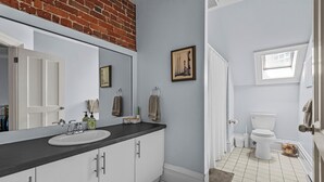 A bathroom with a white sink, mirror, and toilet, a towel rack, and a framed picture on the wall. - Chic Loft suite with WiFi & AC in historic downtown town Halifax near waterfront (Halifax)