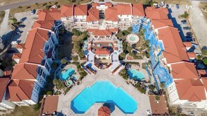 Vue aérienne d’un hôtel comprenant plusieurs bâtiments, une piscine centrale et diverses installations aux alentours.