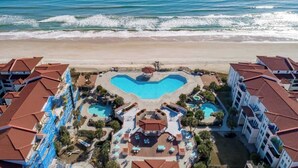 Un complexe hôtelier doté d’une piscine en forme de cœur, de balcons donnant sur la plage et offrant une vue sur la plage.