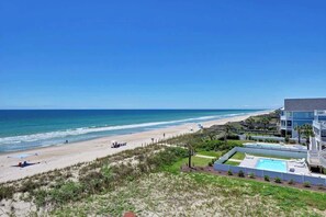 A beach view with a pool area and a building with multiple balconies.