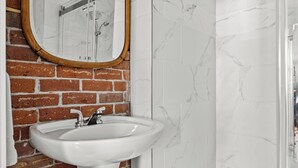 Un baño con un lavamanos blanco, un espejo con marco de madera y una cabina de ducha de vidrio.