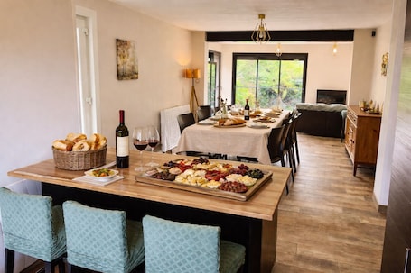 A dining area with a wooden table set for a meal, a wine bottle, and a variety of cheeses and fruits.. Family home - Garden, BBQ & quiet near Paris