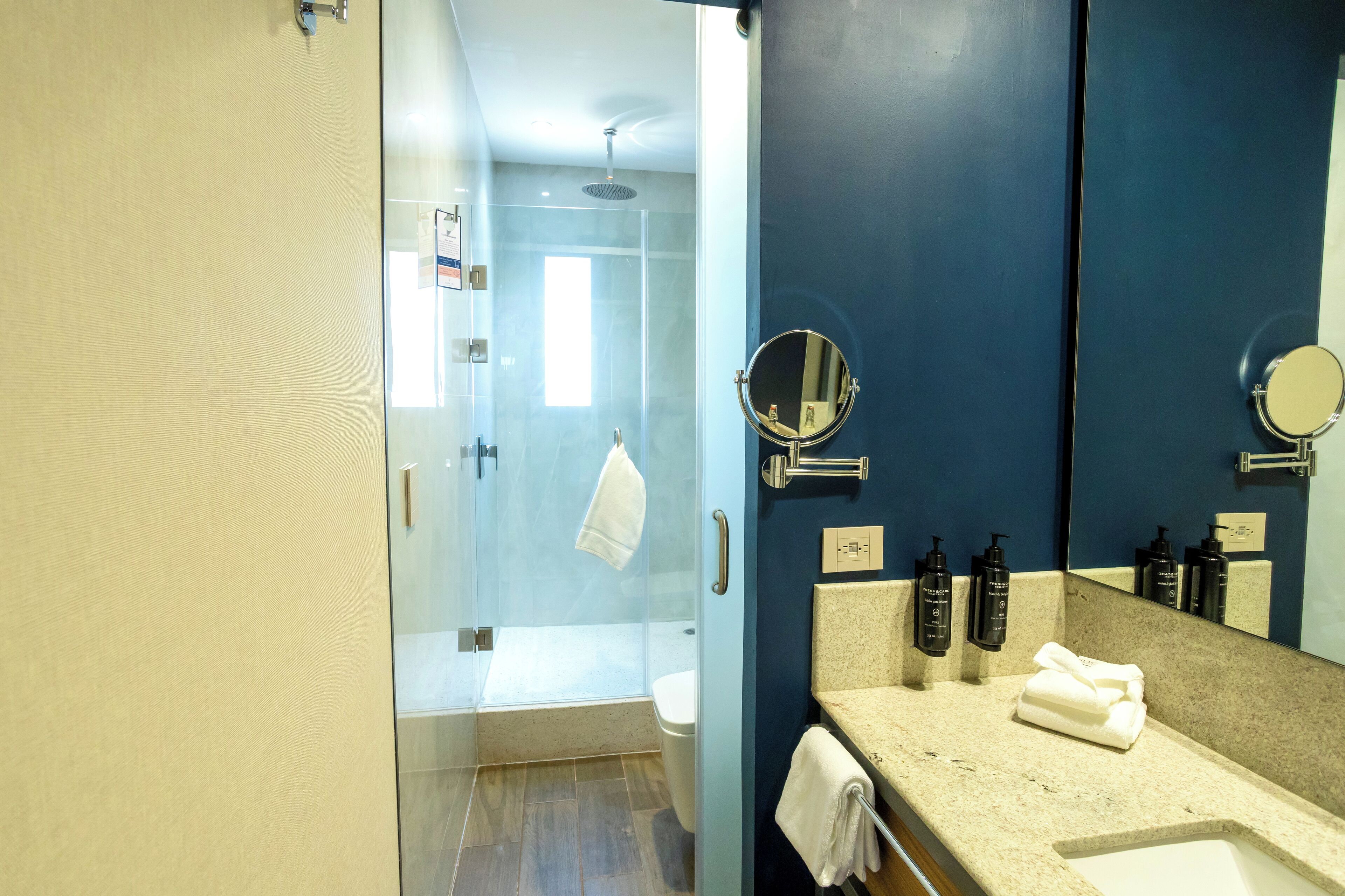 A modern bathroom with a glass shower enclosure, a large mirror, and a beige countertop.
