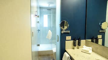 A modern bathroom with a glass shower enclosure, a large mirror, and a beige countertop.