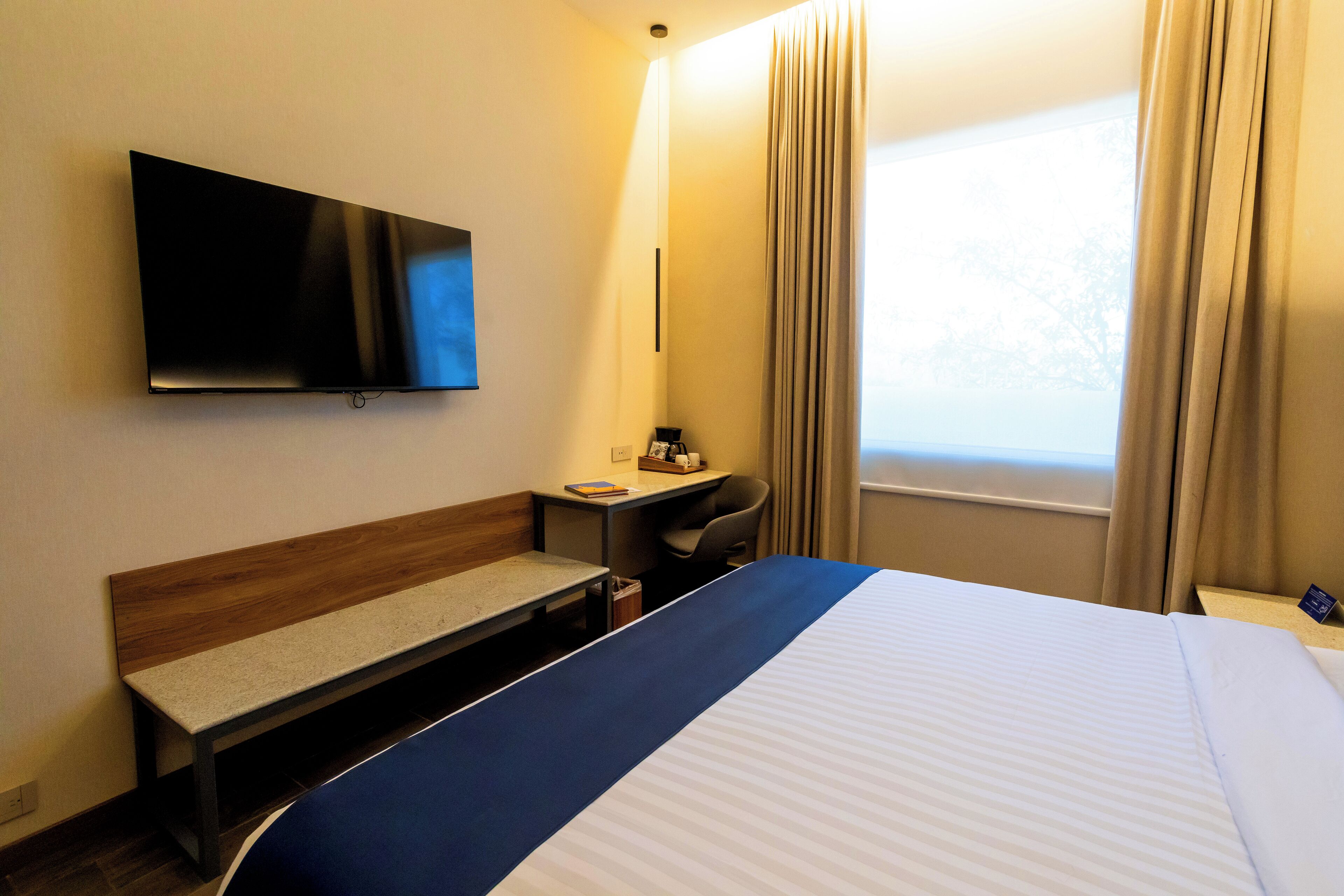 A hotel room with a bed, a desk, a chair, a television, and a window with curtains.