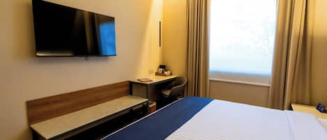 A hotel room with a bed, a desk, a chair, a television, and a window with curtains.