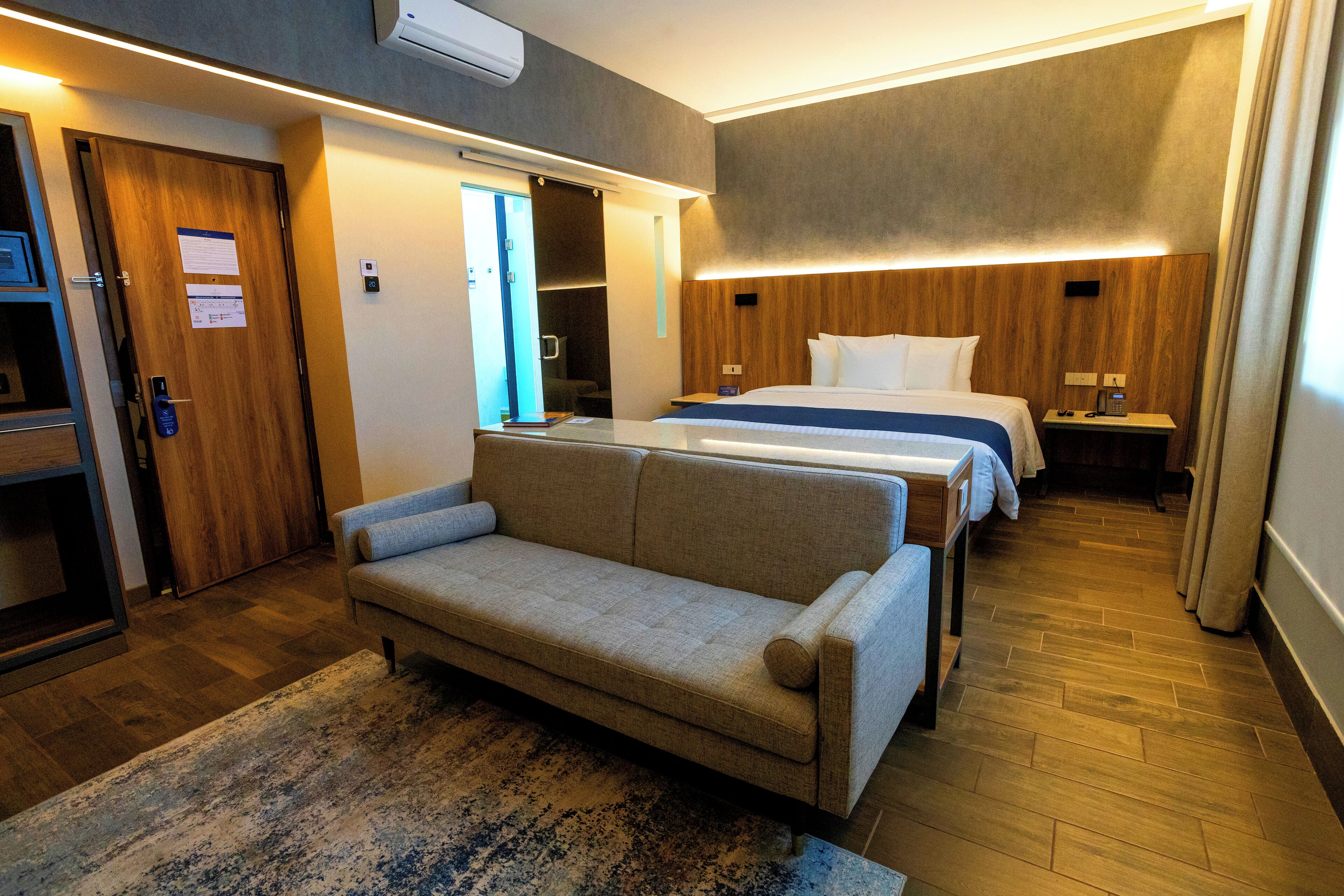 Habitación de hotel con sofá, cama, mesita de noche y suelo de madera.