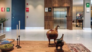Een moderne lobby met een houten receptiebalie, een grote vaas-sculptuur en een gepolijste marmeren vloer.