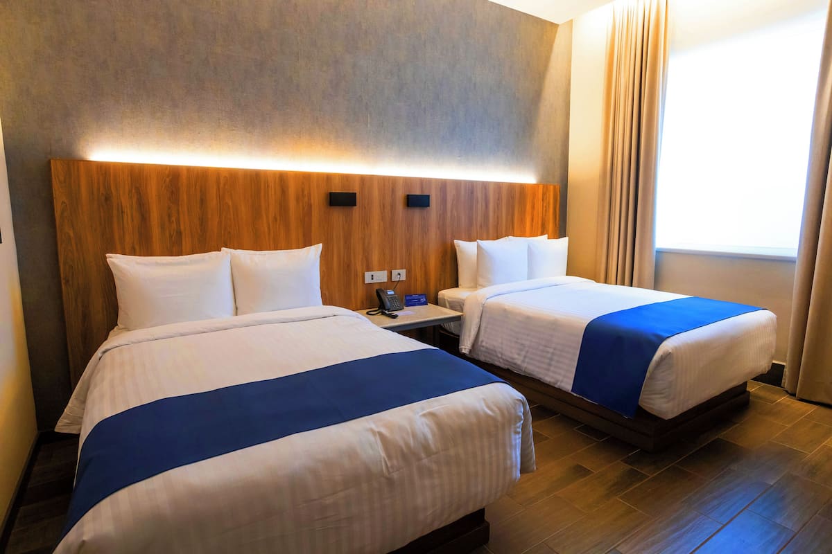 A hotel room with two beds, a wooden headboard, a bedside table with a phone, and a window with curtains.