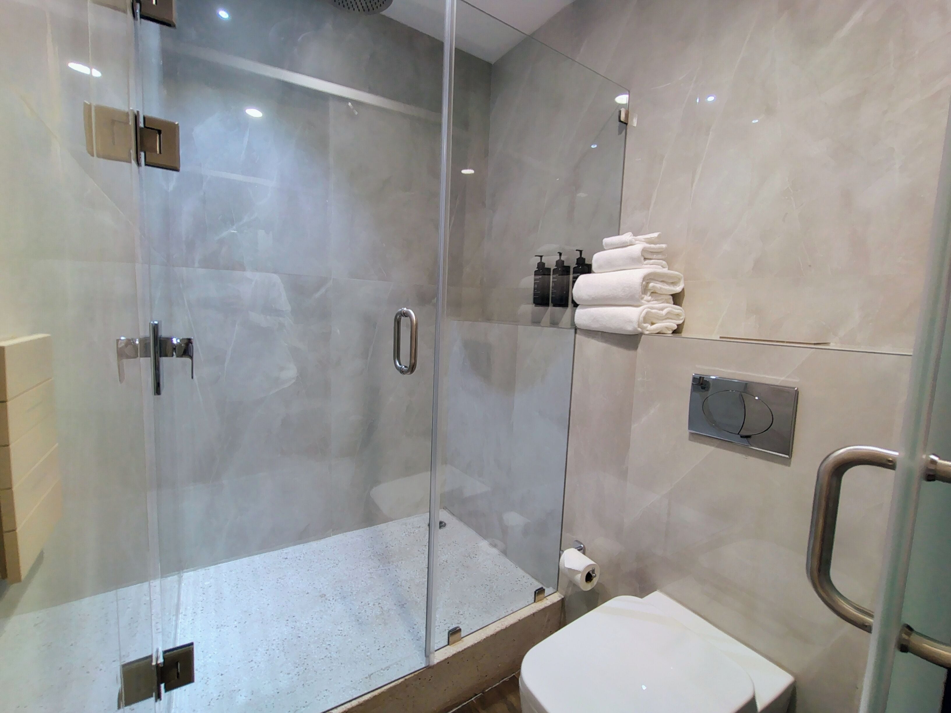 Un baño moderno con ducha de vidrio, inodoro y toallero con toallas dobladas.